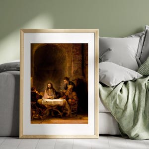May include: A framed print of a religious painting depicting a scene with several figures gathered around a table. The artwork features warm, earthy tones and detailed brushstrokes, creating a classical aesthetic. The setting appears to be an interior with an arched doorway.
