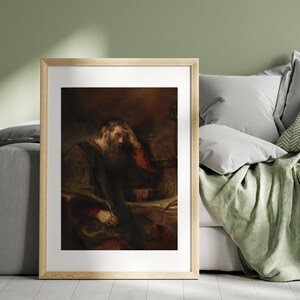 May include: Framed artwork featuring a man with a long beard, dressed in dark robes, resting his head on his hand. The painting has a warm color palette with brown, red, and gold tones. The artwork is displayed in a wooden frame.