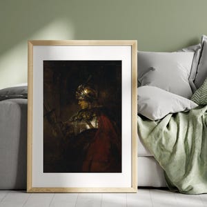 May include: Framed print of a painting depicting a knight in armor holding a sword. The knight wears a golden helmet and a red cloak. The artwork is set against a dark background, with a wooden frame.