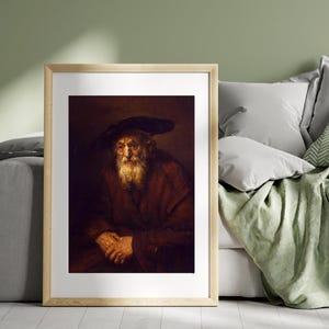 May include: Framed print of an old man in a dark hat and red robe. The portrait features a long white beard and a somber expression. The artwork is displayed in a light wood frame, suitable for home decor.
