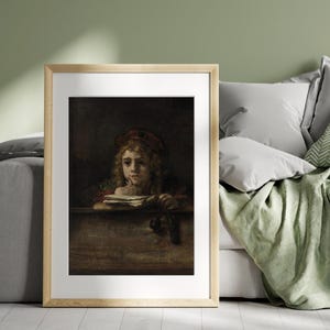 May include: Framed artwork featuring a portrait of a young person with curly hair, wearing a red cap and holding a book. The painting has a dark, moody aesthetic with a wooden frame, displayed on a wall above a bed.