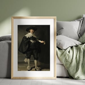 May include: Framed print of a classical portrait. The subject is a person in a black hat, cape, and breeches, with a white lace collar. The person is holding a small piece of paper. The background is a dark, neutral color.