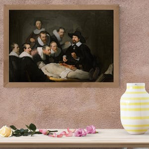 May include: A framed print of Rembrandt's "The Anatomy Lesson of Dr. Nicolaes Tulp" hangs on a pink wall. The painting depicts a group of men gathered around a cadaver. A yellow and white striped vase sits on a wooden table.