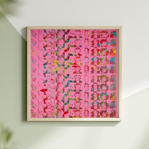 May include: A framed artwork featuring a pink background with a grid of colorful, stylized portraits. The portraits are in various colors, including red, yellow, blue, and green. The frame is a light wood color, and the artwork is displayed on a white wall.