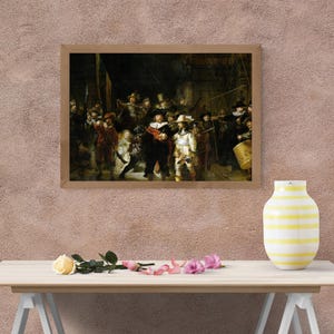 May include: A framed print of Rembrandt's "The Night Watch" hangs on a textured pink wall. The painting depicts a group of figures in historical attire, with a warm color palette. A yellow and white striped vase sits on a wooden table.