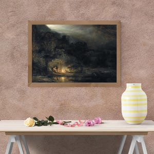 May include: A framed landscape painting depicting a nighttime scene with figures gathered around a fire. The artwork features a dark color palette with a focus on light and shadow, creating a dramatic effect. The frame is made of light-colored wood.