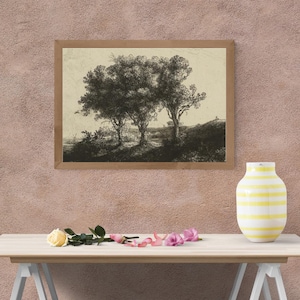 May include: A framed black and white print of three trees in a landscape. The artwork is in a light brown wooden frame. A white vase with yellow horizontal stripes sits on a wooden table, along with a yellow rose and pink flower petals.