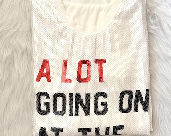 May include: White sequin shirt with the text "A LOT GOING ON AT THE" in red and black lettering.
