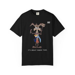 Puede incluir: Camiseta negra con un coyote de dibujos animados sosteniendo un letrero que dice "YUM" y un cuchillo. El coyote sostiene un pájaro de dibujos animados y otros objetos. El texto "IT'S ABOUT DAMN TIME." está impreso debajo.