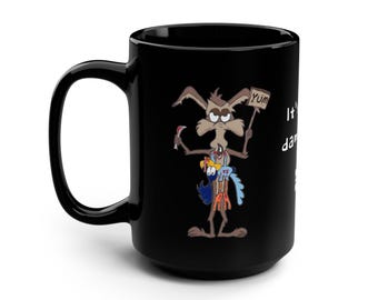 May include: Black ceramic mug featuring a cartoon coyote holding a sign that says "Yum" and a Road Runner. The mug has the text "It's da..." on the side. The coyote is holding a knife and the Road Runner is in his arms.