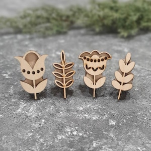 May include: Four wooden floral-themed cutouts. Two are flower-shaped, and two are leaf-shaped. The cutouts are light brown and have intricate details. They are arranged on a gray surface.