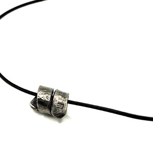 May include: A silver pendant necklace with a twisted, textured design hangs from a black leather cord.