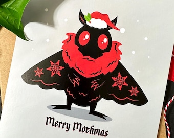 May include: A greeting card with a black moth illustration wearing a Santa hat and red accents. The card reads "Merry Mothmas" in black script. The card is on a brown envelope with red and white twine.