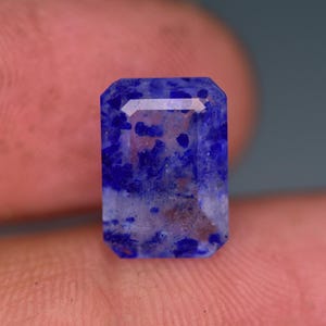 May include: A faceted, blue and white gemstone with a clear, translucent appearance. The gemstone has a rectangular shape with a slightly rounded edge.