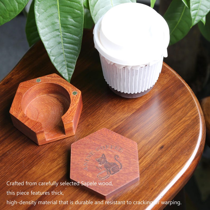 May include: A wooden coaster set and a coffee cup on a wooden table. The coaster set includes a hexagonal coaster and a holder. The coaster has a cat graphic and text. The cup is white with a paper sleeve. The text in the image says: Crafted from carefully selected Sapele wood, this piece features thick, high-density material that is durable and resistant to cracking or warping.
