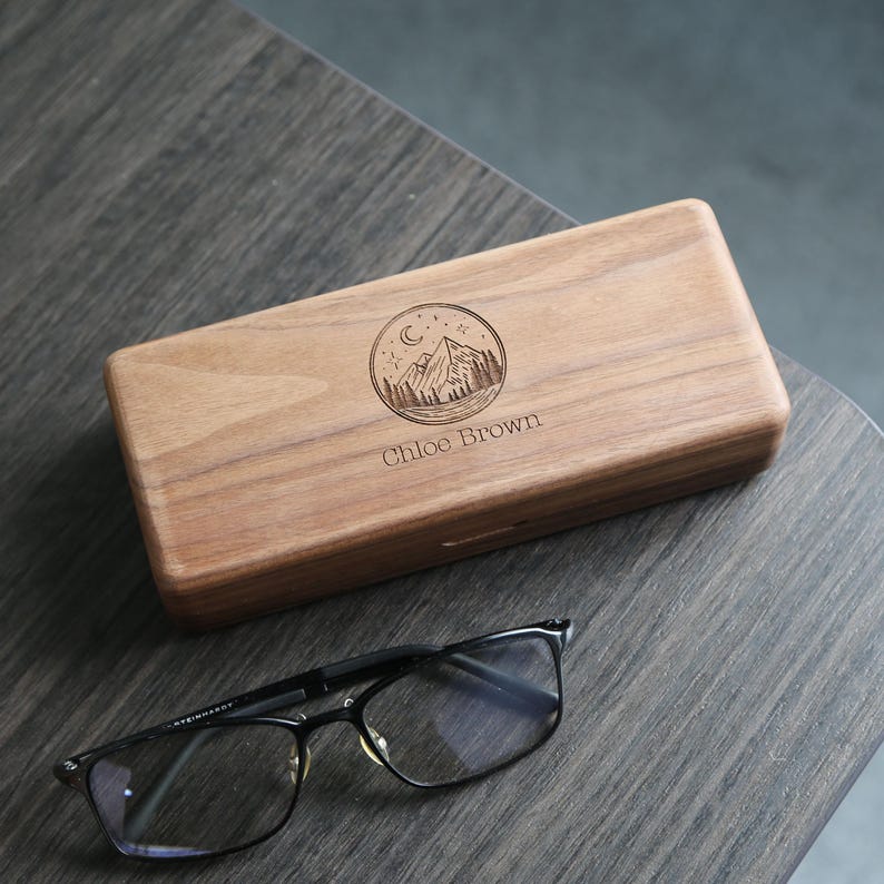 May include: A personalized wooden glasses case with a mountain and moon design. The case is engraved with the name "Chloe Brown".