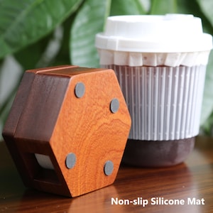May include: A wooden hexagonal coaster with a dark brown finish and four grey non-slip pads. A white and grey reusable coffee cup with a lid is in the background. The text "Non-slip Silicone Mat" is at the bottom.