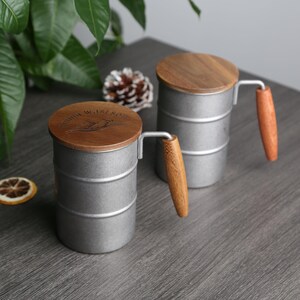 May include: Two silver metal mugs with wooden lids and handles. The lids have the words "Mountain Waistline" engraved on them.