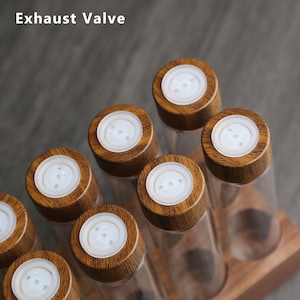 Puede incluir: Conjunto de seis tarros de especias de vidrio con tapas de madera y una base de madera. Las tapas tienen un dispensador blanco de tres agujeros.