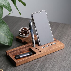 May include: A wooden desk organizer with a phone stand, pen holder, and USB charging ports. The organizer is made of dark brown wood and has a sleek, modern design.