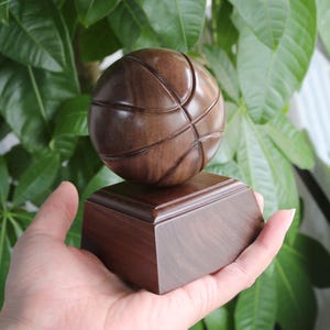 May include: A wooden basketball trophy with a dark brown finish. The basketball is carved with realistic details and sits on a square base.
