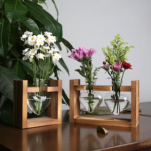May include: Two wooden flower stands with heart-shaped glass vases. The stands are made of natural wood and have a rustic look. The vases are clear glass and are perfect for displaying fresh flowers.