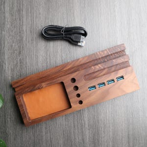 May include: A wooden desk organizer with a built-in USB hub. The organizer has a slot for a phone, a pen holder, and a small tray. The USB hub has five ports.