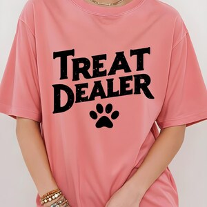 May include: A pink t-shirt with the text "Treat Dealer" in black with a black paw print below the text.
