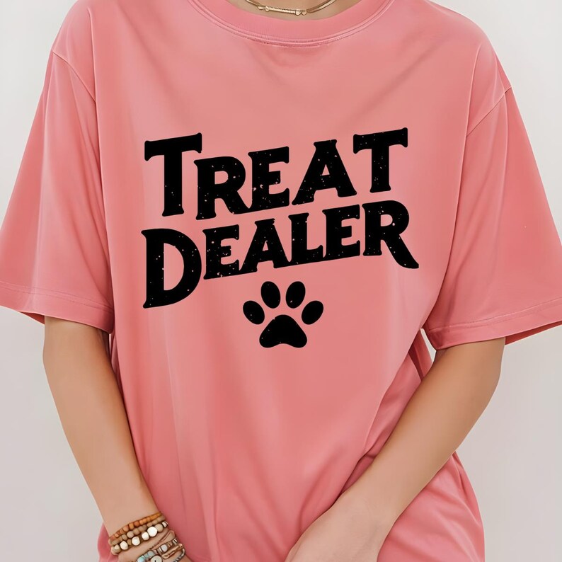 May include: A pink t-shirt with the text "Treat Dealer" in black with a black paw print below the text.