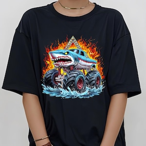 May include: Black t-shirt with a graphic of a blue and white monster truck with a shark head. The truck is driving through water and flames.