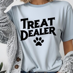 May include: Light blue t-shirt with the text "Treat Dealer" in black with a black paw print below the text.
