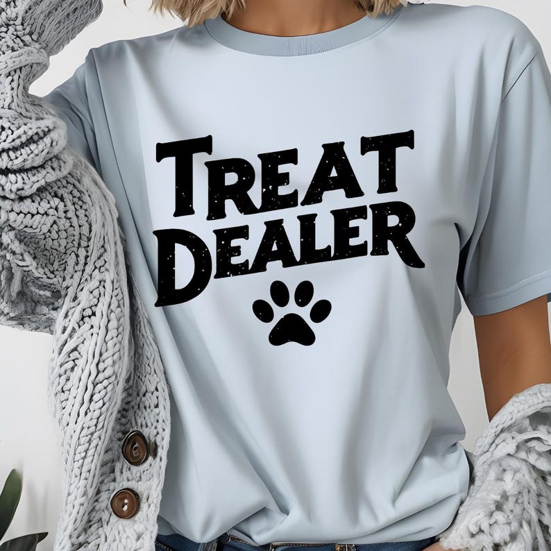 May include: Light blue t-shirt with the text "Treat Dealer" in black with a black paw print below the text.