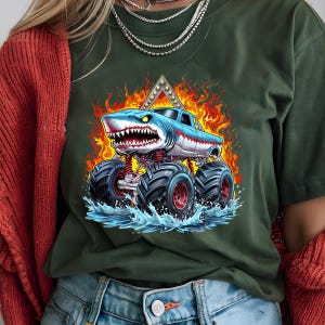 May include: A green t-shirt with a graphic of a blue shark monster truck driving through water with flames behind it.