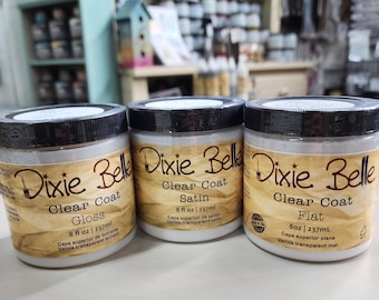 May include: Three clear jars of Dixie Belle Clear Coat in Gloss, Satin, and Flat finishes. Each jar has a black lid and a label with the product name, finish type, and volume of 8 fl oz (237ml).