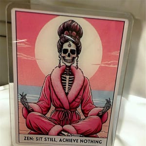 Op de afbeelding: Een badge met een skelet in een roze badjas, zittend in meditatie voor een roze en oranje achtergrond. De tekst "ZEN: SIT STILL, ACHIEVE NOTHING" staat onderaan. De badge is bevestigd aan een transparante plastic houder.