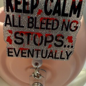 Puede incluir: Un portatarjetas brillante con el texto "KEEP CALM ALL BLEEDING STOPS... EVENTUALLY" en letras negras con detalles de salpicaduras de sangre rojas. El portatarjetas tiene una correa de plástico transparente y un clip metálico.