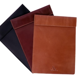 Puede incluir: Tres fundas para portátil de cuero en negro, burdeos y marrón. Las fundas tienen cierre de solapa y están hechas de cuero de alta calidad. La funda marrón tiene el texto "AL" en una fuente estilizada.