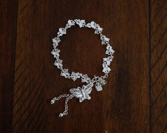 May include: A silver anklet with a butterfly charm and a heart charm. The anklet is made of delicate silver chains and features a series of butterfly-shaped links.