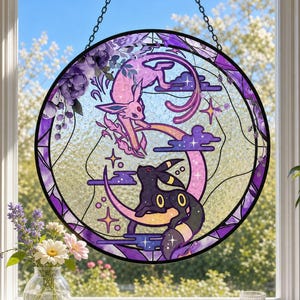 May include: A circular stained glass suncatcher featuring a pink Espeon and a black Umbreon character design. The artwork includes purple floral accents, a crescent moon, and star motifs, all framed within a dark border hanging by a metal chain.