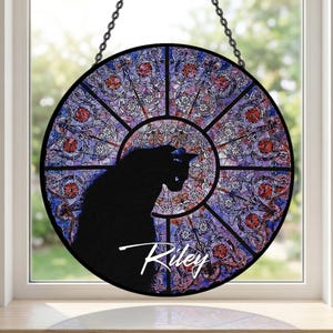 May include: Round stained glass window art featuring a black cat silhouette. The window has a colorful stained glass design with purple, blue, and red hues. The name "Riley" is written in white script below the cat.