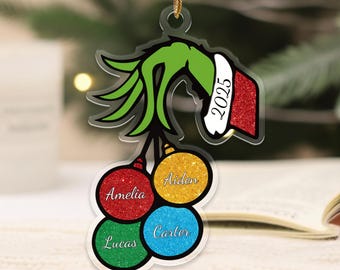 May include: A clear acrylic Christmas ornament featuring a green hand holding a red and white hat with the year 2025. Four colorful ornaments below are labeled with the names Amelia, Aiden, Lucas, and Carter.