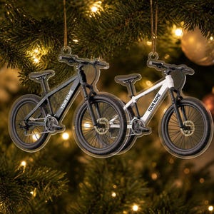 May include: Two flat, hanging ornaments shaped like mountain bikes, one black and one white. Each bike frame features the text YOUR NAME in a sans-serif font. The ornaments are suspended by gold strings and have detailed wheels and handlebars.