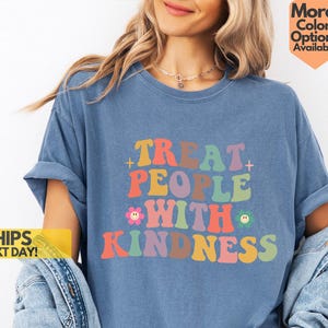 May include: A blue t-shirt with the text "Treat People With Kindness" in rainbow colors. The text is in a retro font style with a flower and smiley face graphic.