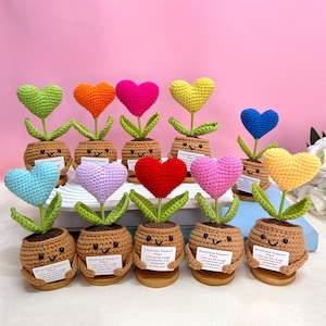 May include: A collection of ten crocheted heart-shaped flower pots with smiling faces. Each pot has a small sign that reads "Emotional Support Plant. Life can be tough sometimes, but remember, you are you!"