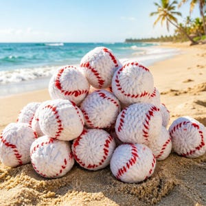 Może przedstawiać: Stos białych piłek do baseballu z czerwonymi szwami na piaszczystej plaży. Piłki do baseballu są wykonane z miękkiego, teksturowanego materiału. W tle widać morze i palmy.