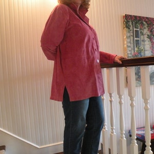 May include: A woman wearing a pink long-sleeved shirt with a button-up front and a side slit. She is standing on a staircase with a white railing.