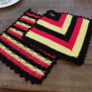 May include: Two handmade crochet potholders. One features red, yellow, and black stripes, while the other has a V-shaped design in the same colors. Both have a black scalloped edge and a loop for hanging. Kitchen decor.