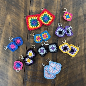 May include: A collection of crocheted square earrings in various colors and patterns, including rainbow, pink, purple, blue, yellow, and black. The earrings are all made with a single crochet stitch and have a simple, minimalist design.