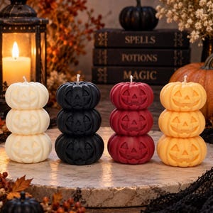 May include: Four stacks of three carved pumpkin candles in white, black, red, and orange. Each candle features a jack-o'-lantern face with triangular eyes and a jagged mouth. The candles are arranged in a row on a circular stone surface.