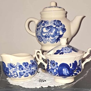 Può includere: Un set di tre tazze da tè in ceramica blu e bianca con motivi floreali. Il set comprende una teiera, un creamer e una zuccheriera con coperchio.